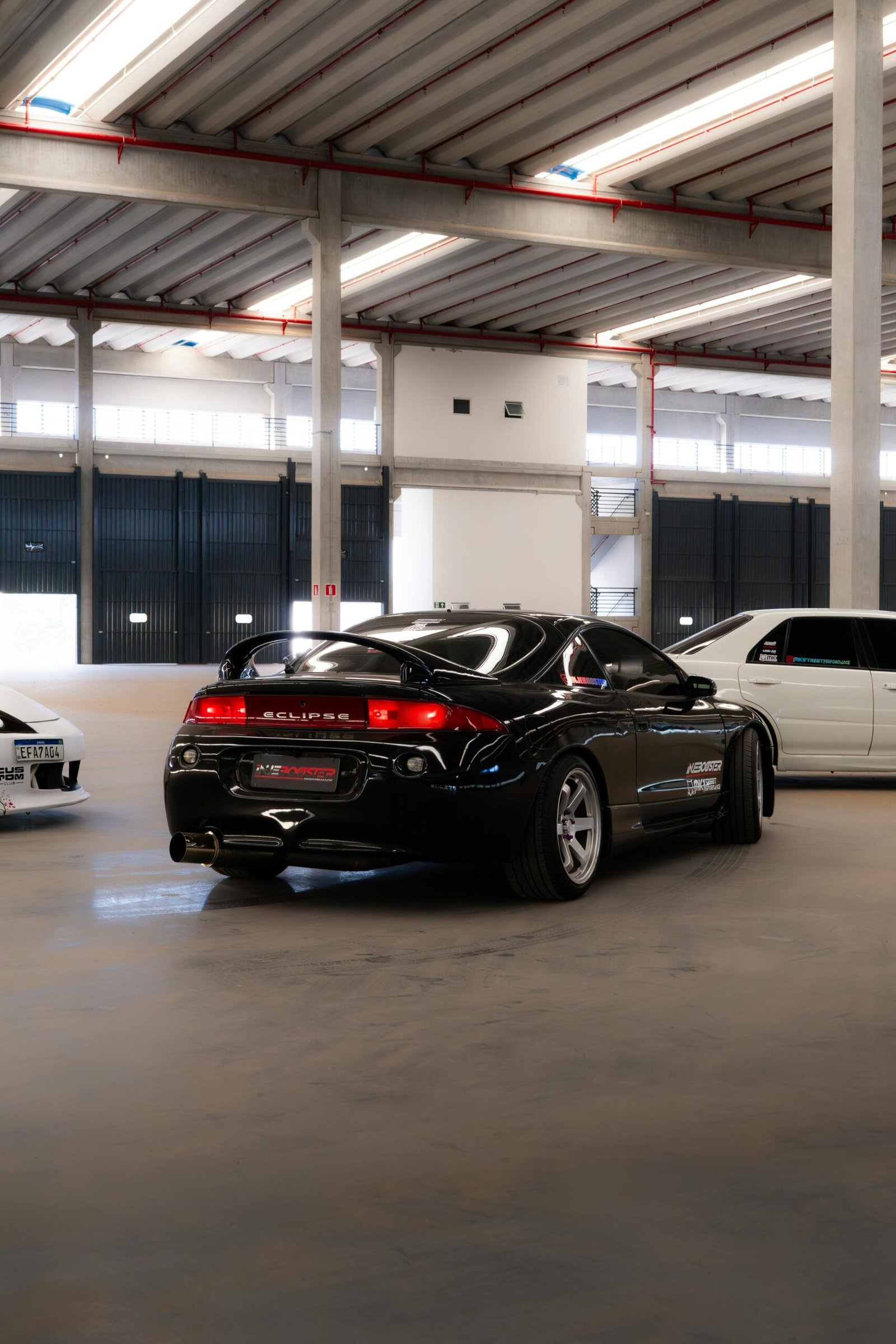 A black Mitsubishi Eclipse parked in an industrial-style indoor garage under soft lighting.